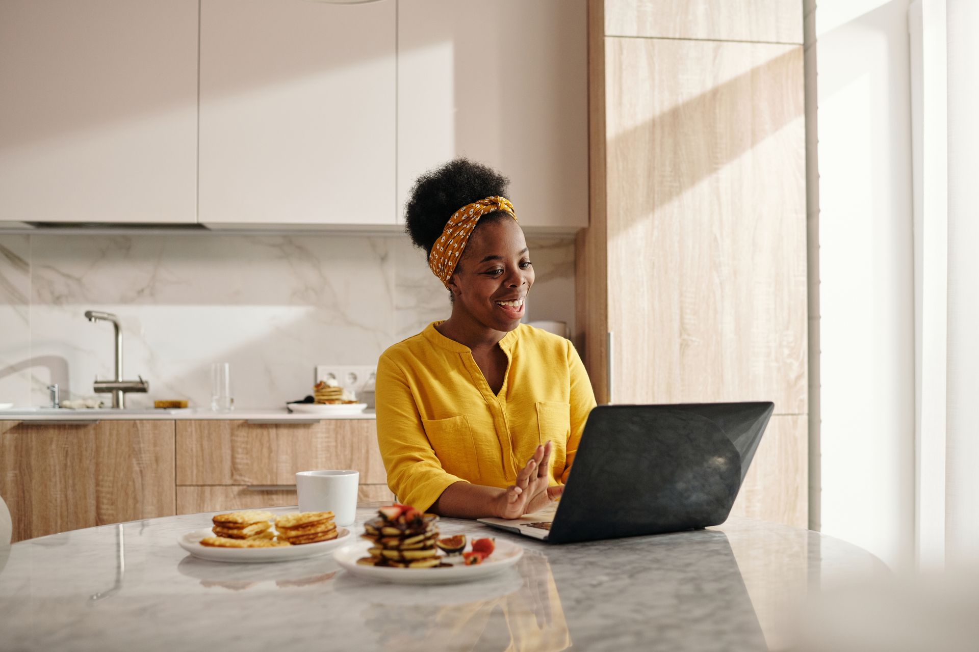 A shop owner laughing with delight at her laptop while writing her newsletter over breakfast